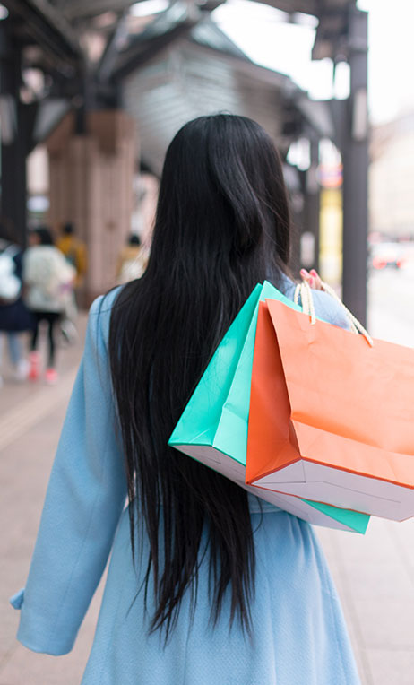 Japan – View of a woman from behind carrying shopping bags over her shoulder.